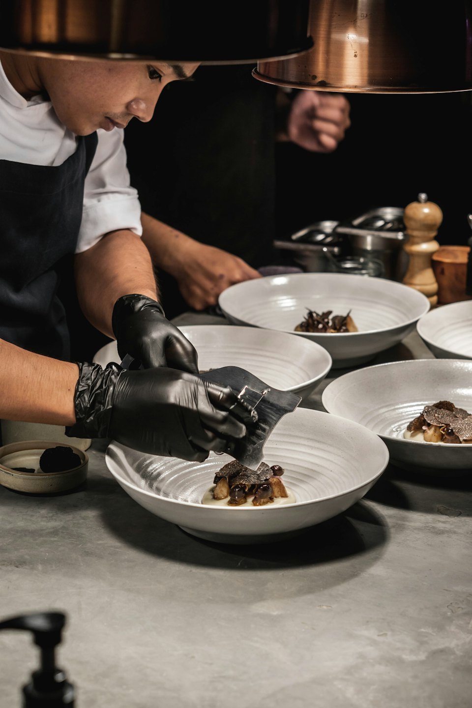 Chef plating dishes and shaving truffles in a professional kitchen.