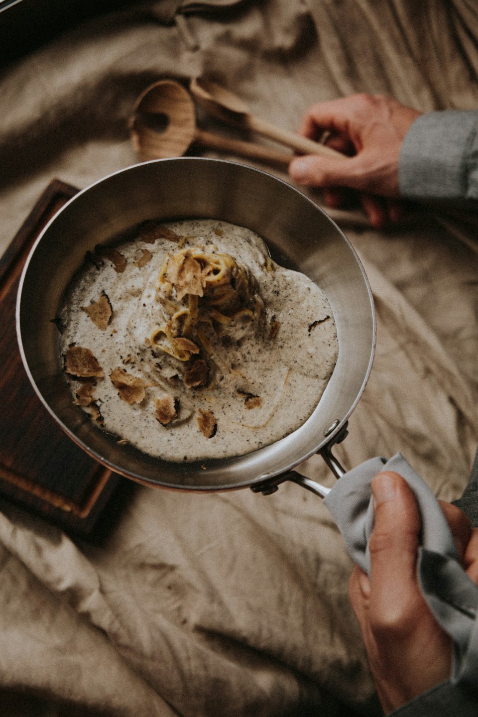 Hands serving creamy truffle pasta from a metal pan.