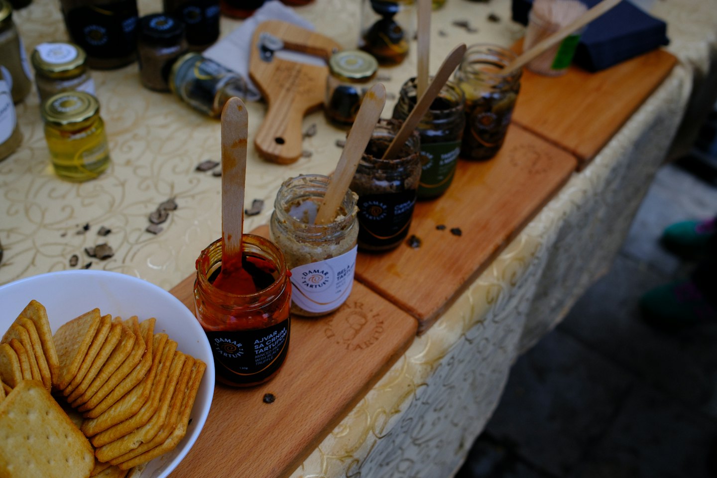 Glass jars of truffle spreads with tasting spoons on wooden boards.